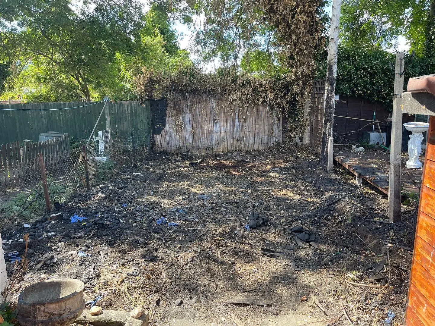 The same corner cleared down to scorched bare earth, with small pieces of charcoal and plastic debris remaining.