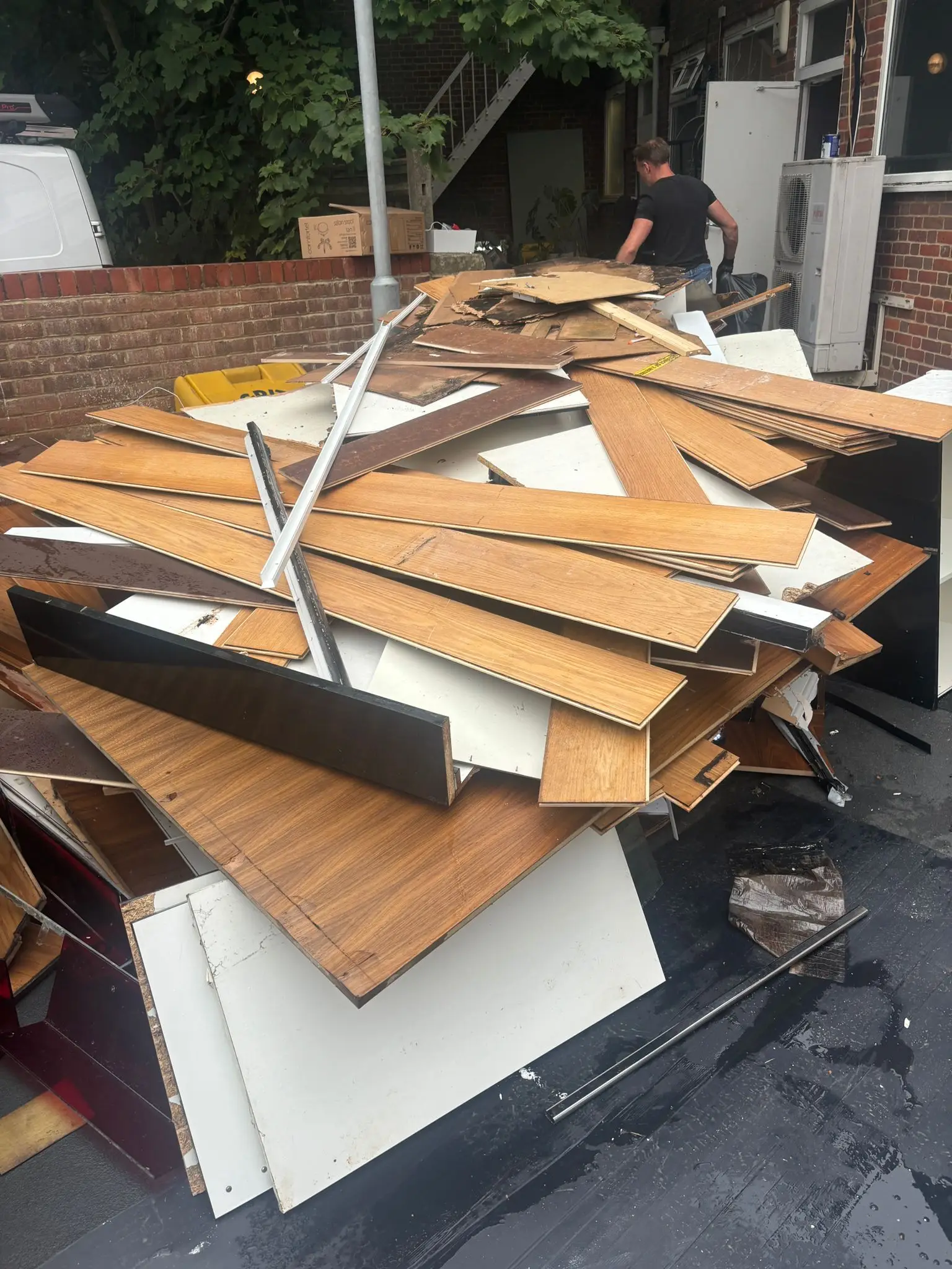 Stripped-out laminate flooring, worktops and wall panels piled on tarmac outside a commercial building.