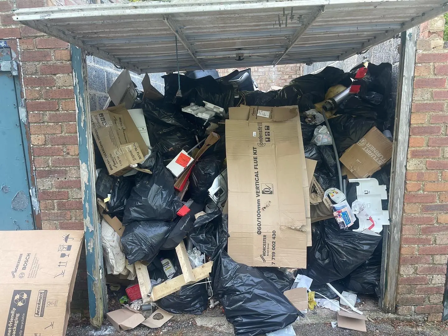 Garage filled with bagged household waste and cardboard before clearance.