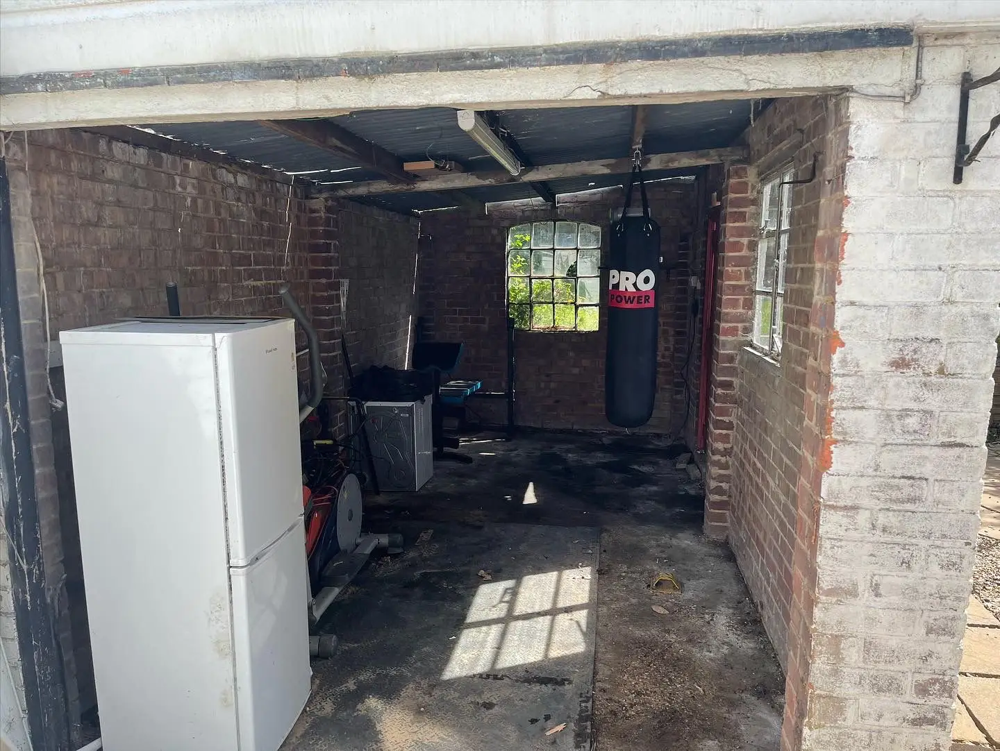 The same garage with the waste removed and the floor swept, the fridge-freezer, washing machine, cross-trainer and punchbag still in place.
