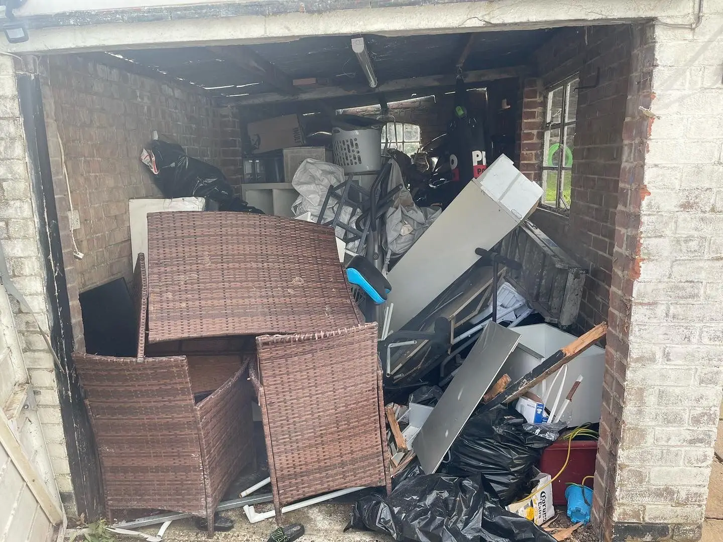 Garage packed to the door with rattan garden furniture, a chest freezer, a filing cabinet, bagged waste and broken timber.