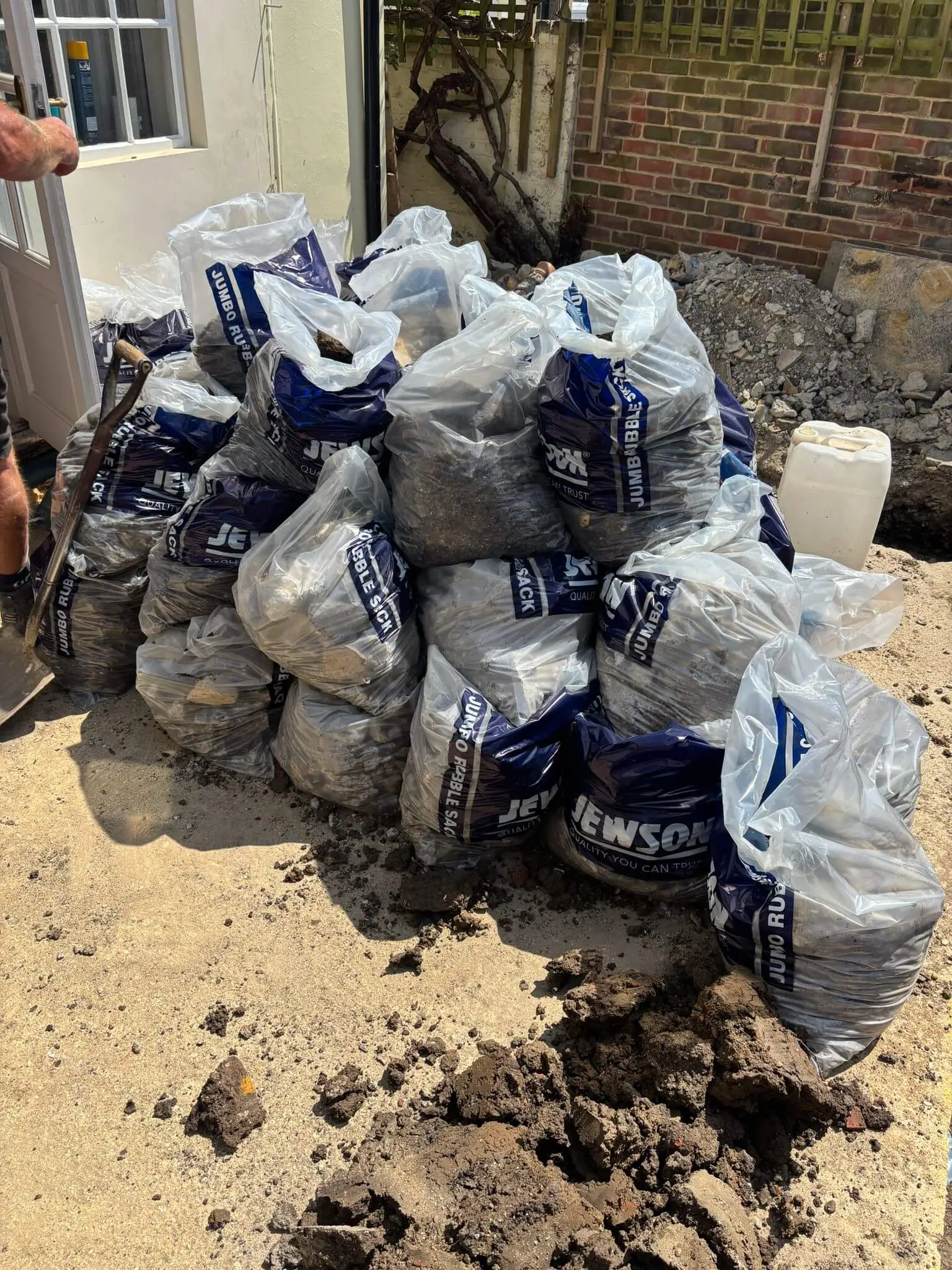 Heap of filled aggregate sacks of rubble on excavated ground beside a house, ready for collection.