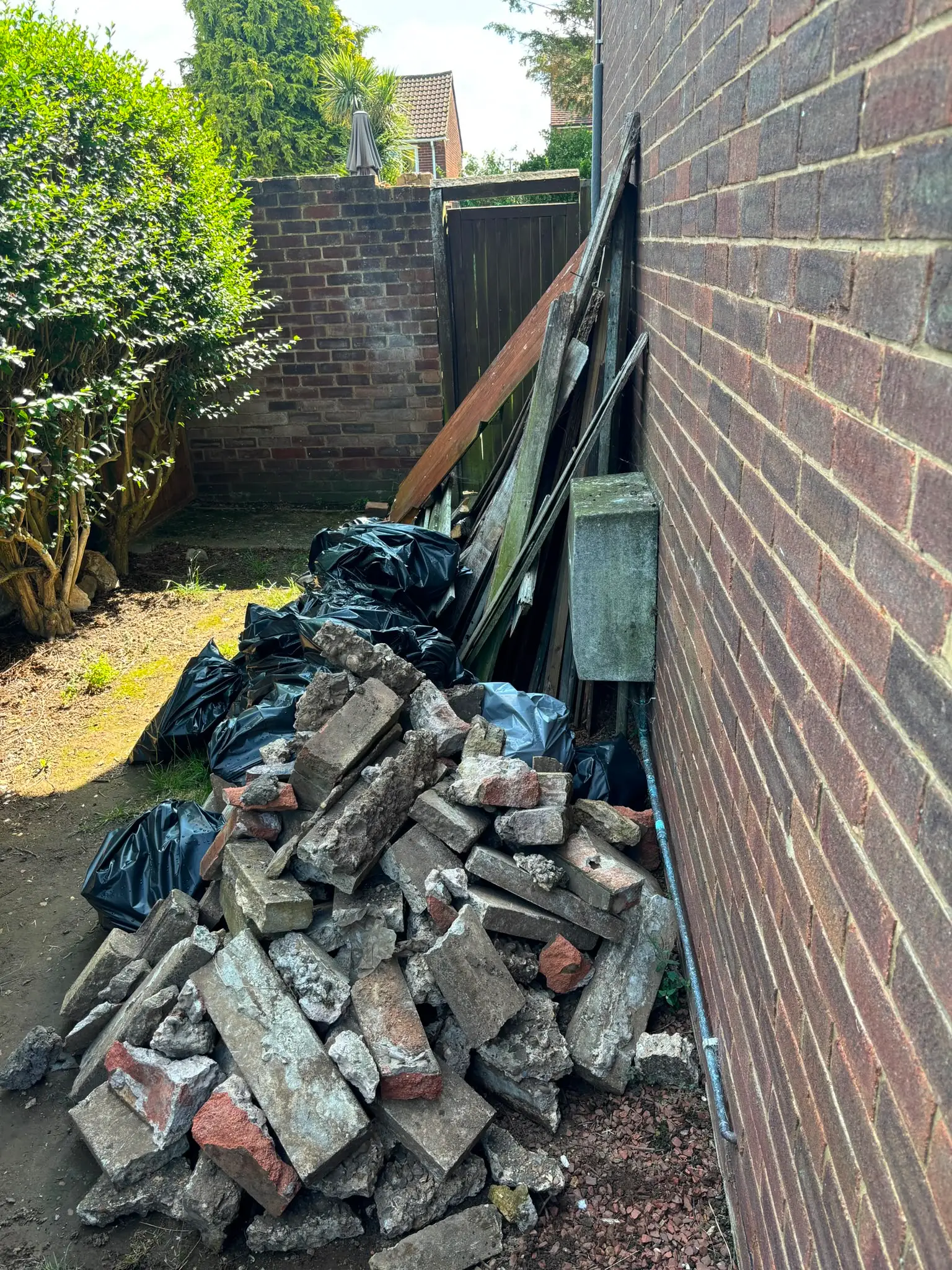 Broken bricks and concrete piled against a house wall, with bagged waste and timber behind.