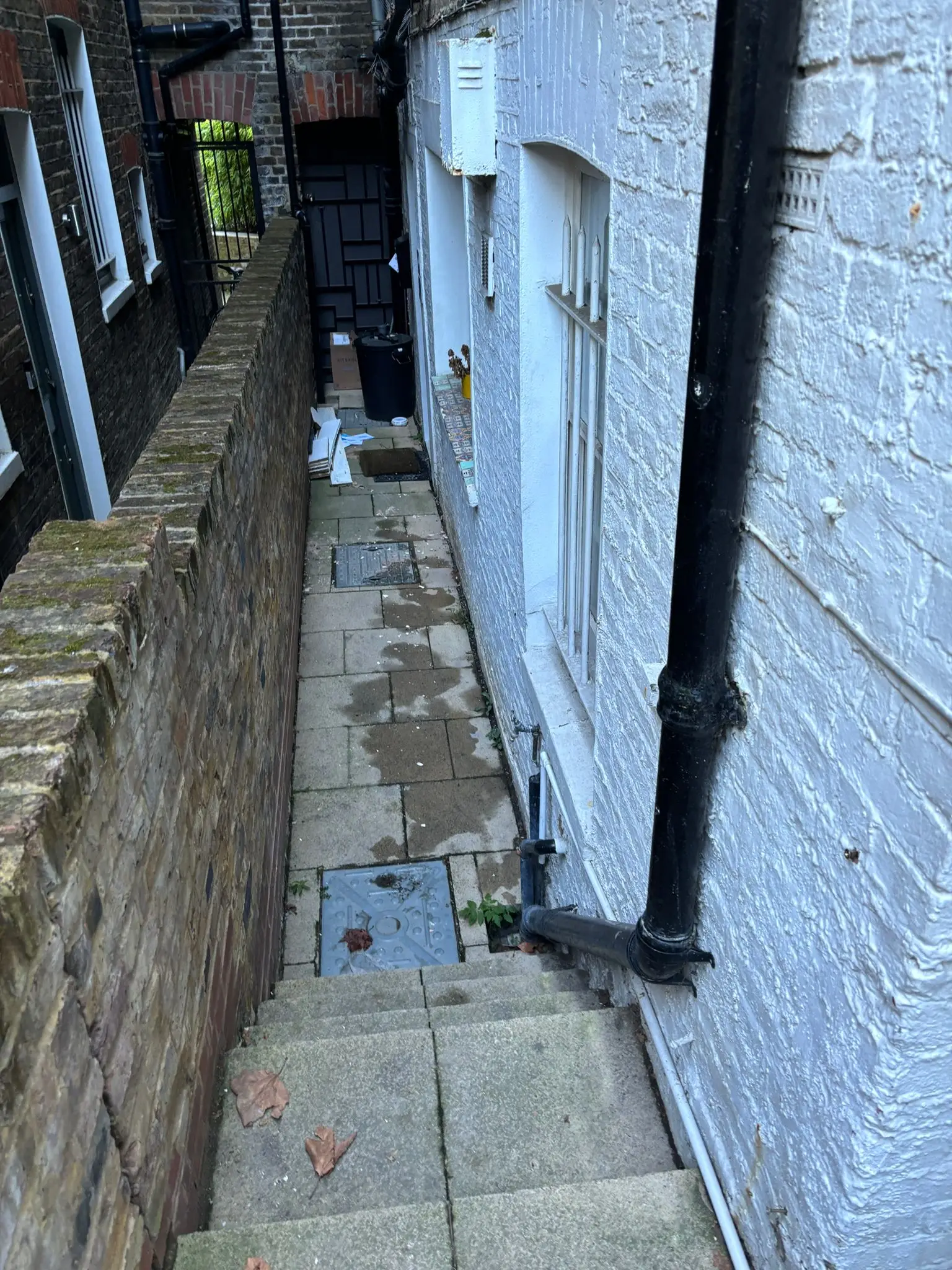 The same passage cleared and swept, with the drain covers visible and a bin and two boards left at the end.