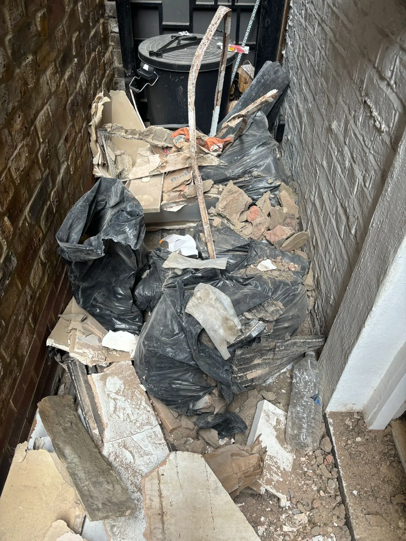 Side passage filled with rubble, broken plasterboard and bagged builders waste before clearance.