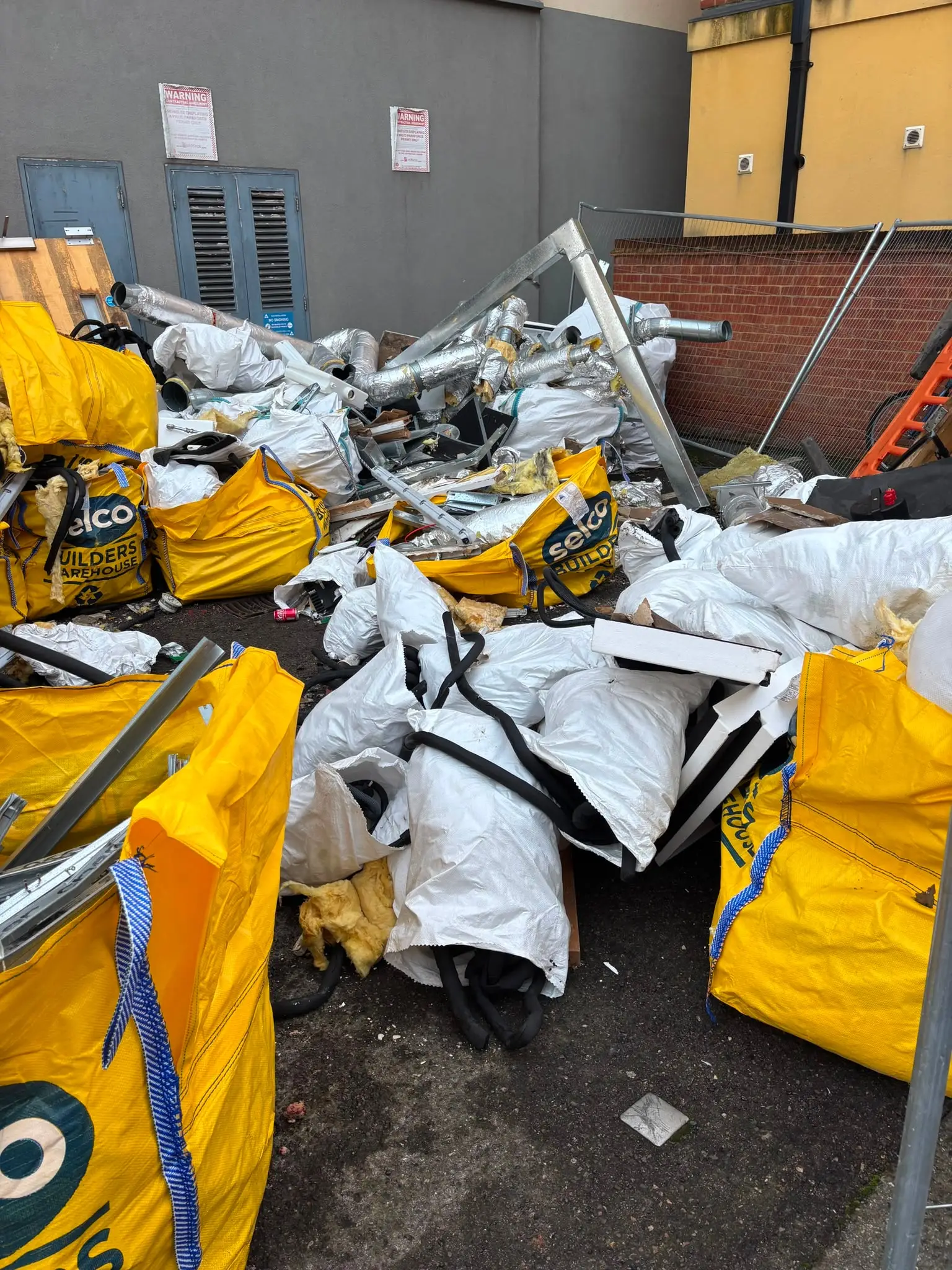 Yellow builders bags and bulk sacks filled with metal ducting and strip-out waste in a commercial yard.